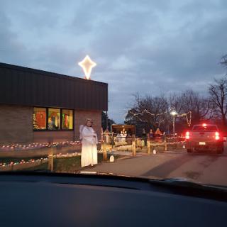 A view of a decorated commercial building during the evening, with holiday lights and vehicles in the vicinity.