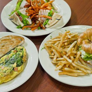 A table set with an omelette, a turkey sandwich with fries, and a fresh salad.