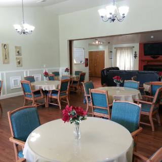 A cozy dining area with round tables, blue chairs, and floral centerpieces under elegant chandeliers.