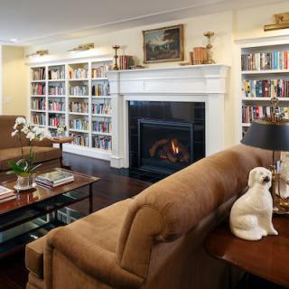 A cozy living room with a fireplace, surrounded by bookshelves and comfortable seating.