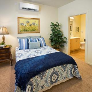 A cozy bedroom with a bed, air conditioner, and decorative elements such as a lamp and plant.