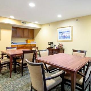 A well-lit meeting room featuring several wooden tables and upholstered chairs, with artwork on the wall.
