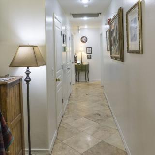 A well-lit hallway adorned with artwork and a standing lamp, featuring tiled flooring and a small table at the far end.