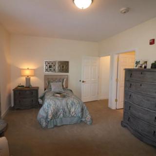 A cozy bedroom with a neatly made bed, wooden dresser, and soft lighting.