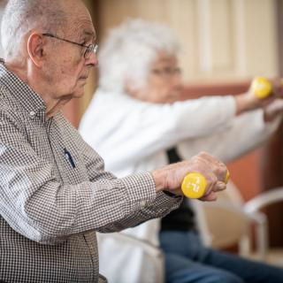 Elderly individuals participating in a seated exercise session with small weights.