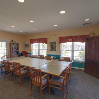A spacious conference room with a large table and wooden chairs, featuring natural light from multiple windows.