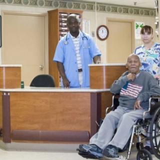 A doctor and nurse stand behind a patient in a wheelchair at a hospital reception area.