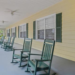 A peaceful porch with green rocking chairs against a yellow wall, perfect for relaxation.