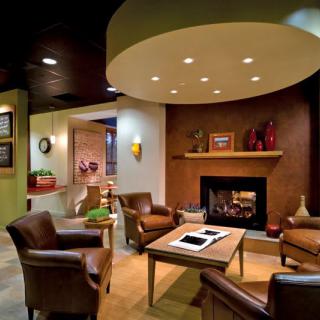 A modern and cozy living room featuring a fireplace, comfortable armchairs, a wooden table, and ambient lighting.