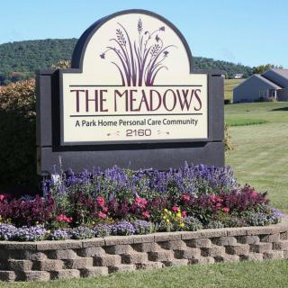 A well-maintained sign for 'The Meadows' personal care community surrounded by vibrant flowers.