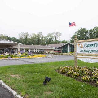 The image shows a healthcare facility with a prominent sign and an American flag in the front, surrounded by greenery.