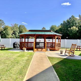 A serene outdoor space featuring a wooden gazebo surrounded by lush grass and a clear blue sky.