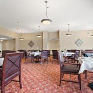 A spacious dining room with neatly arranged tables and chairs, featuring elegant light fixtures and patterned carpet.