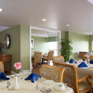 A cozy dining room with neatly arranged tables and chairs, featuring blue napkins and floral decor.