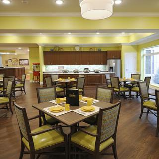 A modern dining area with neatly arranged tables and chairs, featuring warm yellow walls and wooden flooring.