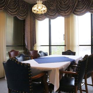 An elegant dining room with a table, surrounded by chairs, adorned with a chandelier and curtains.