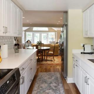 A modern kitchen with white cabinets and stainless steel appliances leading to a dining area with hardwood flooring.