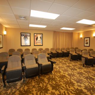 A cozy home theater room with multiple rows of plush seating and framed posters on the walls.
