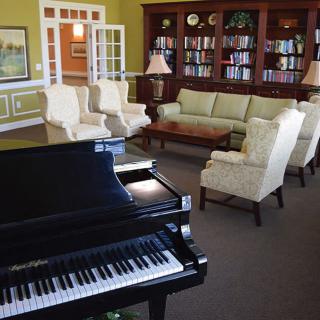 A cozy living room with a grand piano, comfortable seating, and a bookshelf.