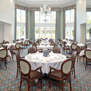 A beautifully arranged formal dining room with round tables, elegant chairs, and a chandelier.