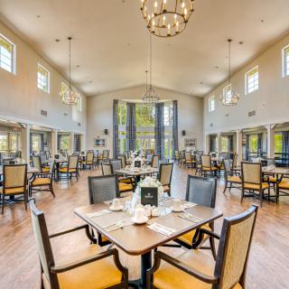 A spacious and elegantly designed dining area with neatly arranged tables and chairs, illuminated by chandeliers.