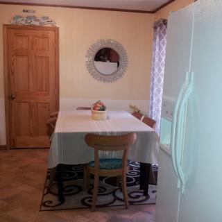A cozy kitchen dining area with a table and chairs, featuring a mirror on the wall and a refrigerator in view.