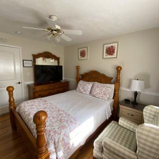 A cozy bedroom with a wooden double bed, ceiling fan, and a television on a dresser.