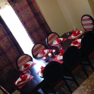 A dining room with a table set for guests, featuring red accents and striped chairs.