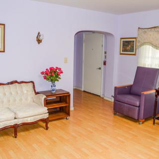 A cozy living room with a vintage couch and armchair, featuring a wooden floor and decorative flowers on a side table.