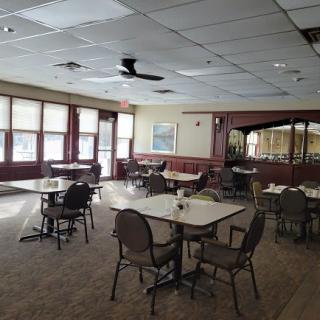 An empty dining room with several tables and chairs, well-lit by large windows.