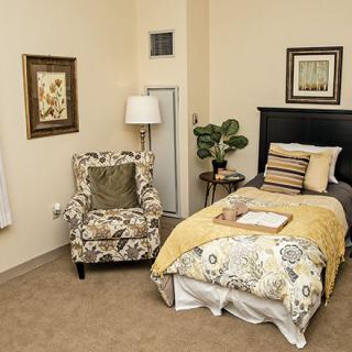 A cozy bedroom with a single bed, floral armchair, and decorative elements.
