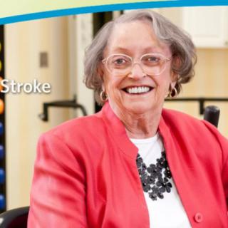 An elderly woman in a red jacket smiles while seated indoors.
