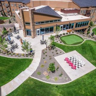 An aerial view of a modern building with landscaped gardens, featuring a large outdoor chessboard and green pathways.