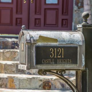 A metal mailbox with the address '3121 Castle Heights' in front of stone steps leading to a red door.