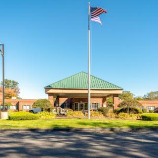 A well-maintained building with a flag flying in front, surrounded by lush landscaping under a clear blue sky.