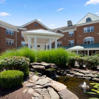 A scenic view of a building surrounded by lush greenery and a tranquil pond.