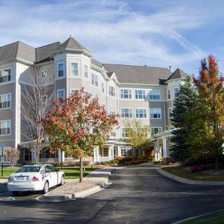 A residential building surrounded by trees with autumn foliage and a parked car in front.