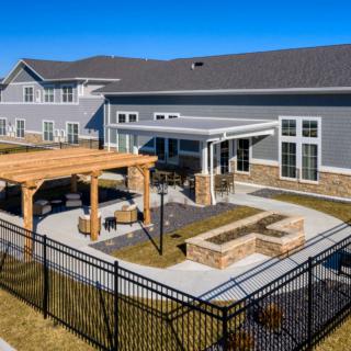 A modern residential building features a spacious backyard with a pavilion, patio, and fire pit under sunny skies.