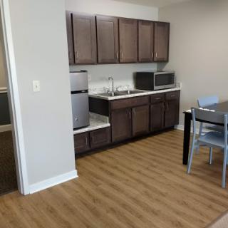 A modern apartment kitchen featuring wooden cabinets, stainless steel appliances, and a dining area.