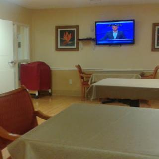 A simple interior room featuring tables and chairs, with a television mounted on the wall.