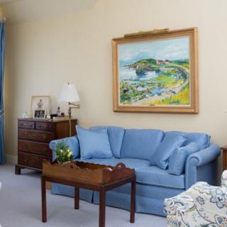 A cozy living room featuring a blue sofa, landscape painting, and wooden furniture.