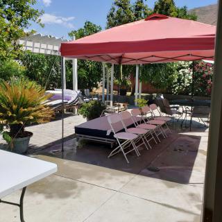 An outdoor patio set up with tables and chairs under a red canopy, ready for a gathering on a sunny day.