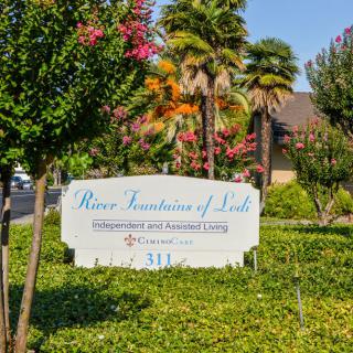 An outdoor sign for 'Rose Fountain of Life' surrounded by trees and landscaping.