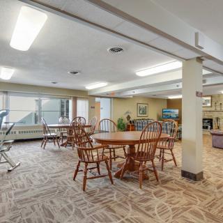 A spacious room with wooden tables and chairs, carpeted flooring, and exercise equipment in the corner.