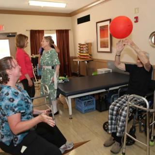 A group of people engaged in a physical therapy session, playing with a red ball, including one person in a wheelchair.