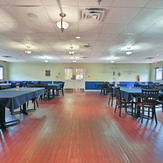 A spacious dining area with neatly arranged tables and chairs, featuring a wooden floor and soft lighting.
