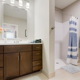 A modern bathroom with a wooden vanity, mirror, and a shower with a blue-striped curtain.