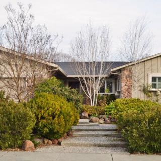 A suburban house with a landscaped front yard, featuring trees and shrubbery along a stone pathway.