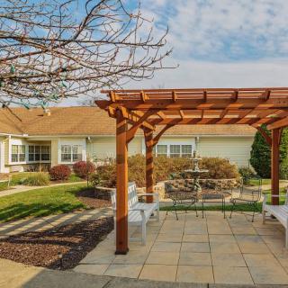 A cozy outdoor patio with a wooden pergola and seating area, surrounded by well-maintained landscaping.