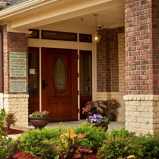 A welcoming entrance with a wooden door surrounded by brick walls and landscaped plants.